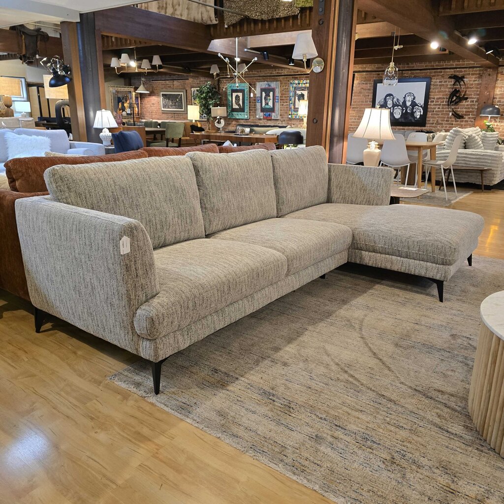 Beige sectional sofa in a showroom setting with wooden flooring and other furniture.