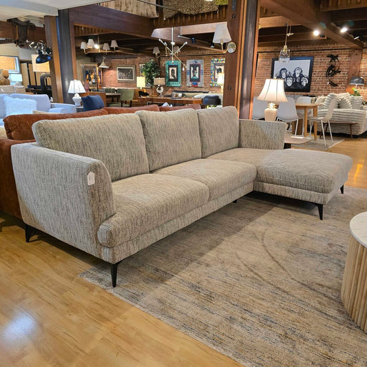 Beige sectional sofa in a showroom setting with wooden flooring and other furniture.