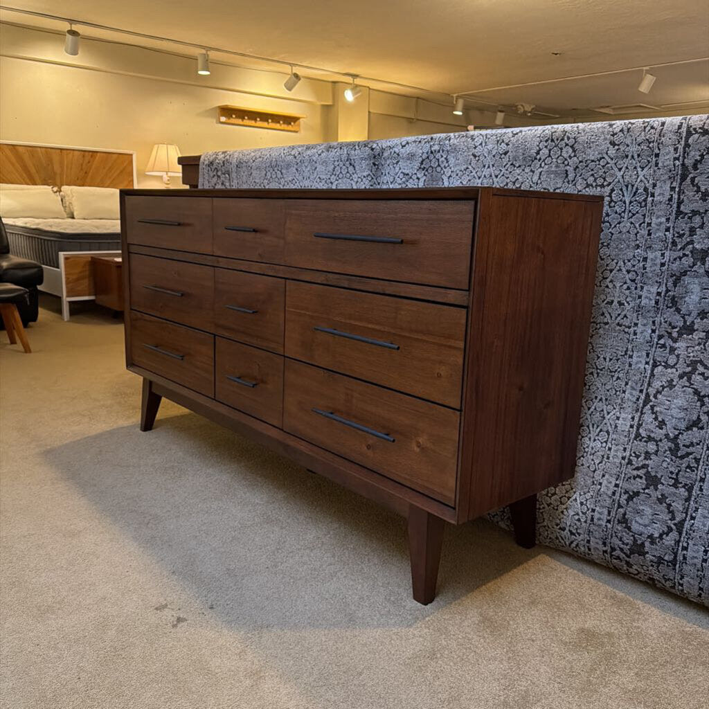 Wooden dresser in a room with a bed and lamp in the background