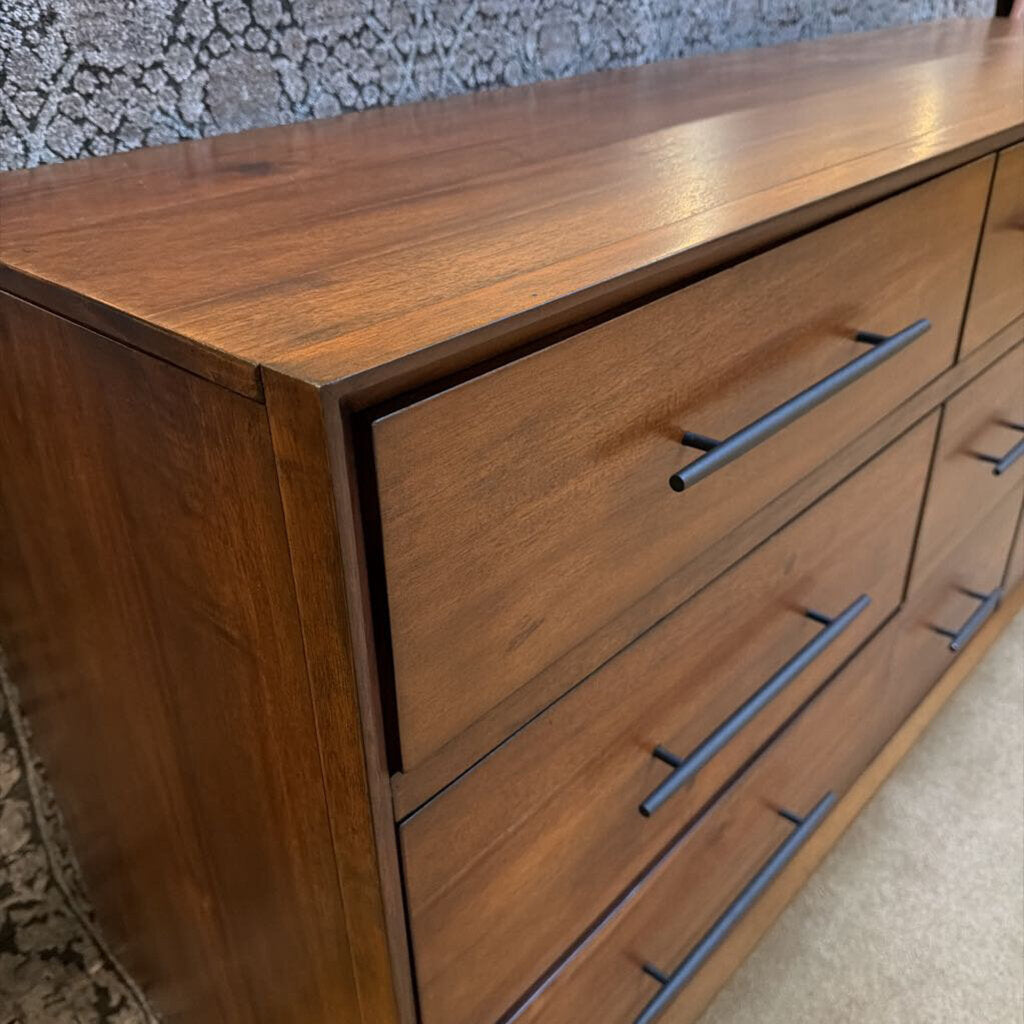 Wooden dresser with four drawers and metal handles against a textured wall.