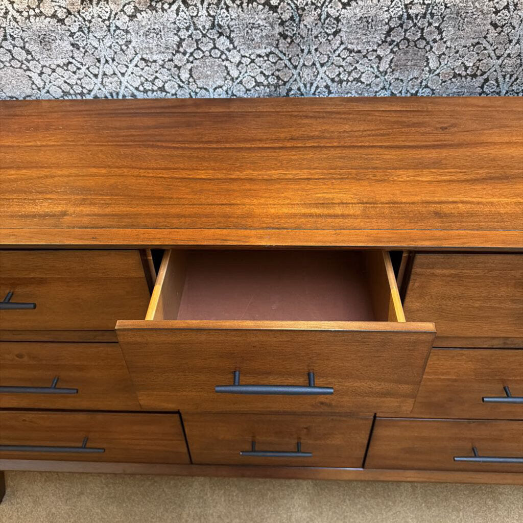 Wooden dresser with open drawer against a patterned wall.