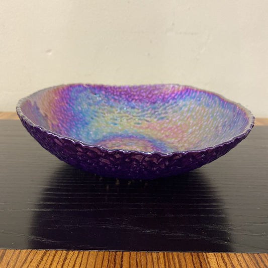 Iridescent glass bowl on a dark surface with a neutral background