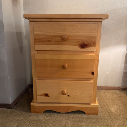 Wooden dresser with three drawers against a plain wall.