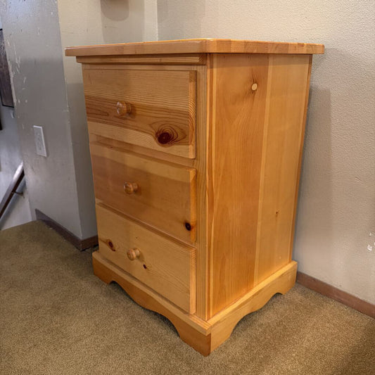 Wooden dresser with three drawers against a wall.