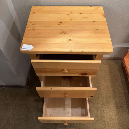 Wooden nightstand with a single drawer open on a carpeted floor.