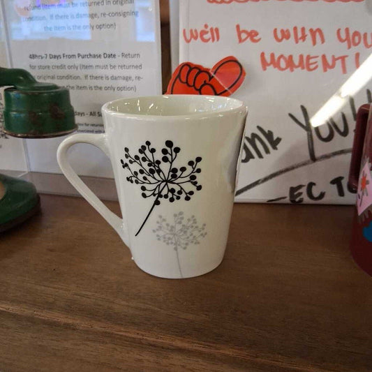 White mug with black floral design on a wooden surface, with a blurred background