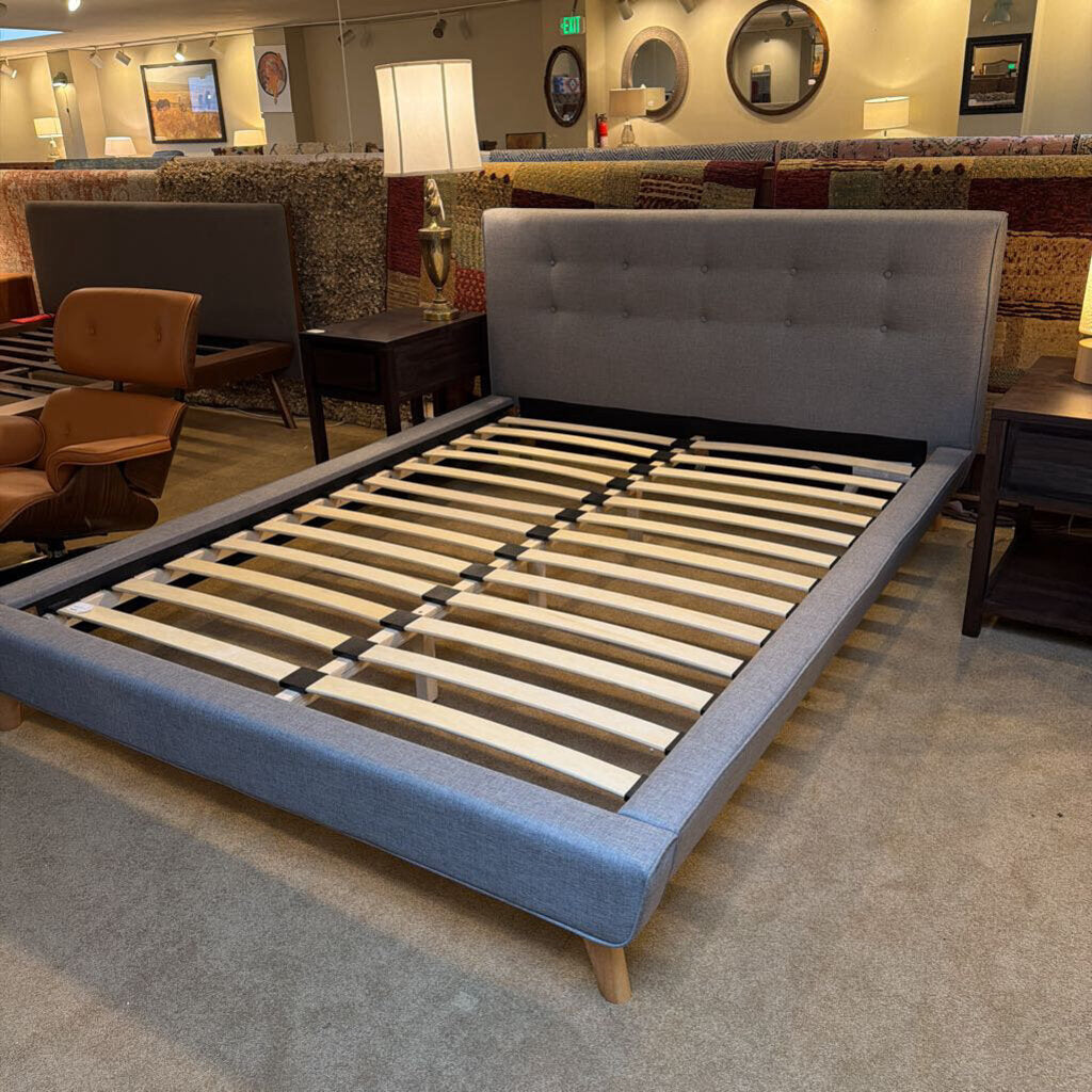 Gray upholstered bed frame with wooden slats in a showroom setting