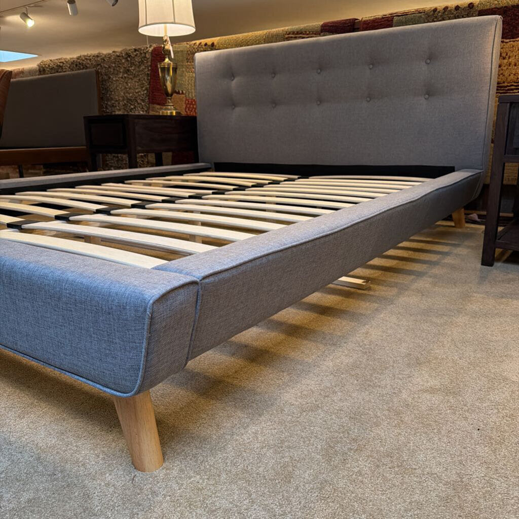 Gray upholstered bed frame with wooden slats on a carpeted floor.