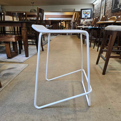 White metal bar stool in a furniture store with wooden tables and chairs in the background.