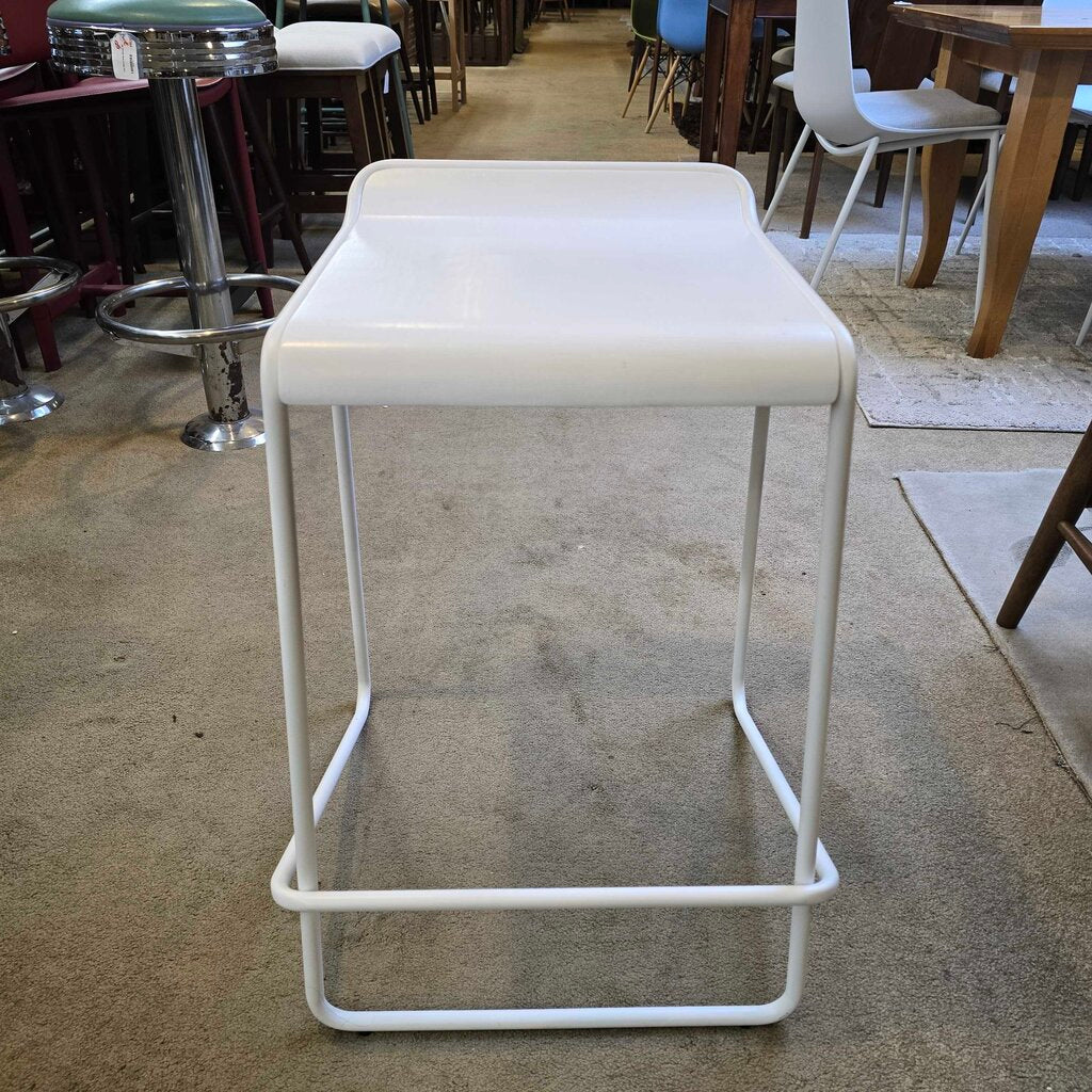 White bar stool on a concrete floor with a blurred background of a cafe setting.