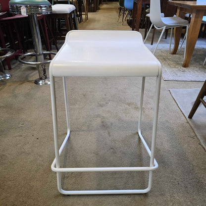 White bar stool on a concrete floor with a blurred background of a cafe setting.