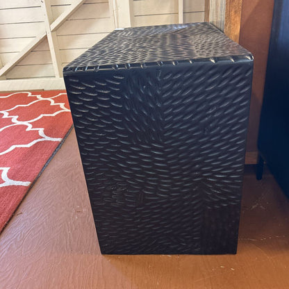 Black textured box on a wooden floor with a red patterned rug