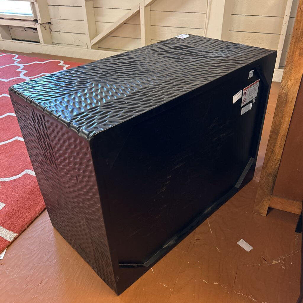Black textured box on a wooden floor with a red patterned rug