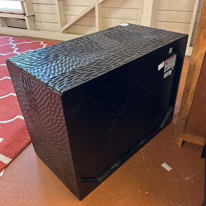 Black textured box on a wooden floor with a red patterned rug