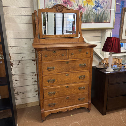 Wooden dresser with mirror against a wooden wall with floral decorations.