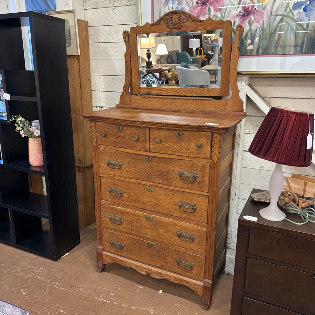 Wooden dresser with mirror in a room setting with furniture and decor.