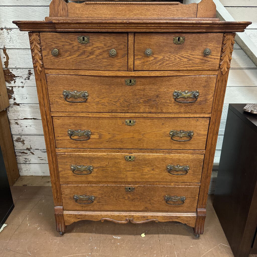 Wooden dresser with multiple drawers against a rustic wooden wall.