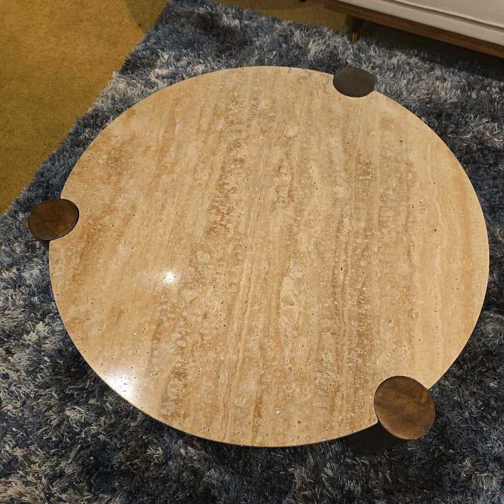 Round wooden table with four metal legs on a textured floor