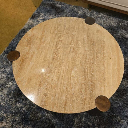 Round wooden table with four metal legs on a textured floor