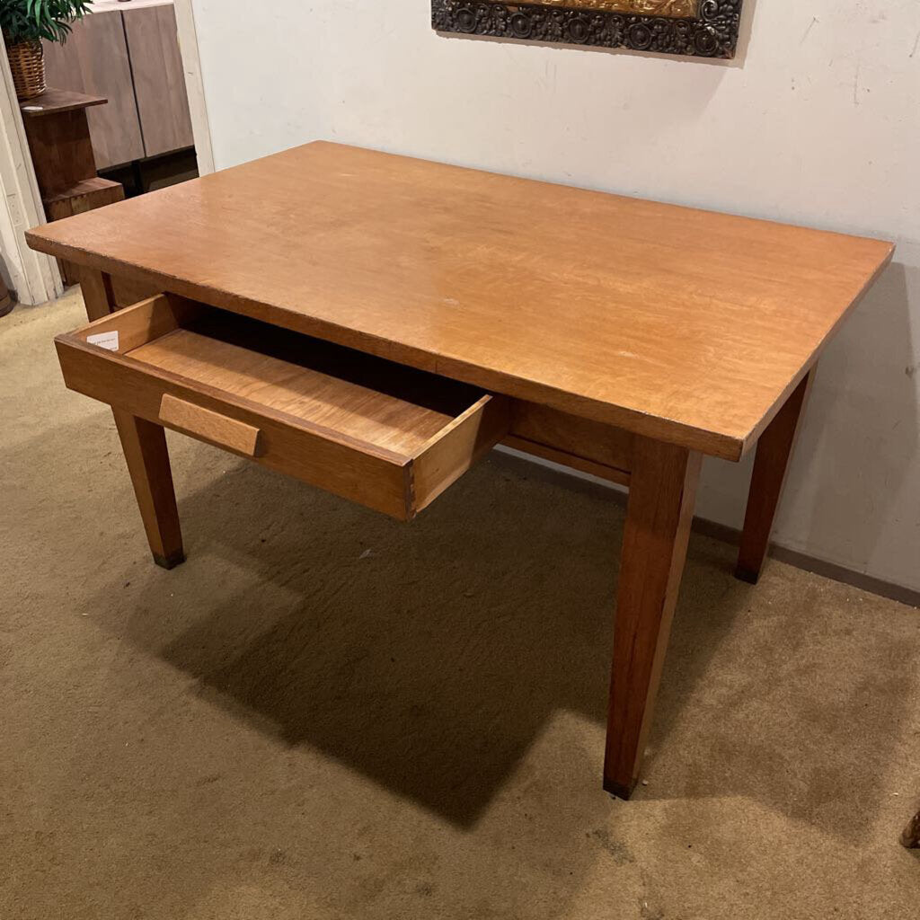 Wooden desk with a drawer in a room with carpeted floor and white walls.
