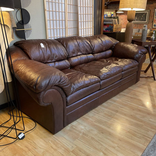 Brown leather sofa in a room with wooden flooring and decorative elements.