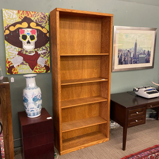 Wooden bookshelf in a room with a vase, typewriter, and framed pictures on the wall.
