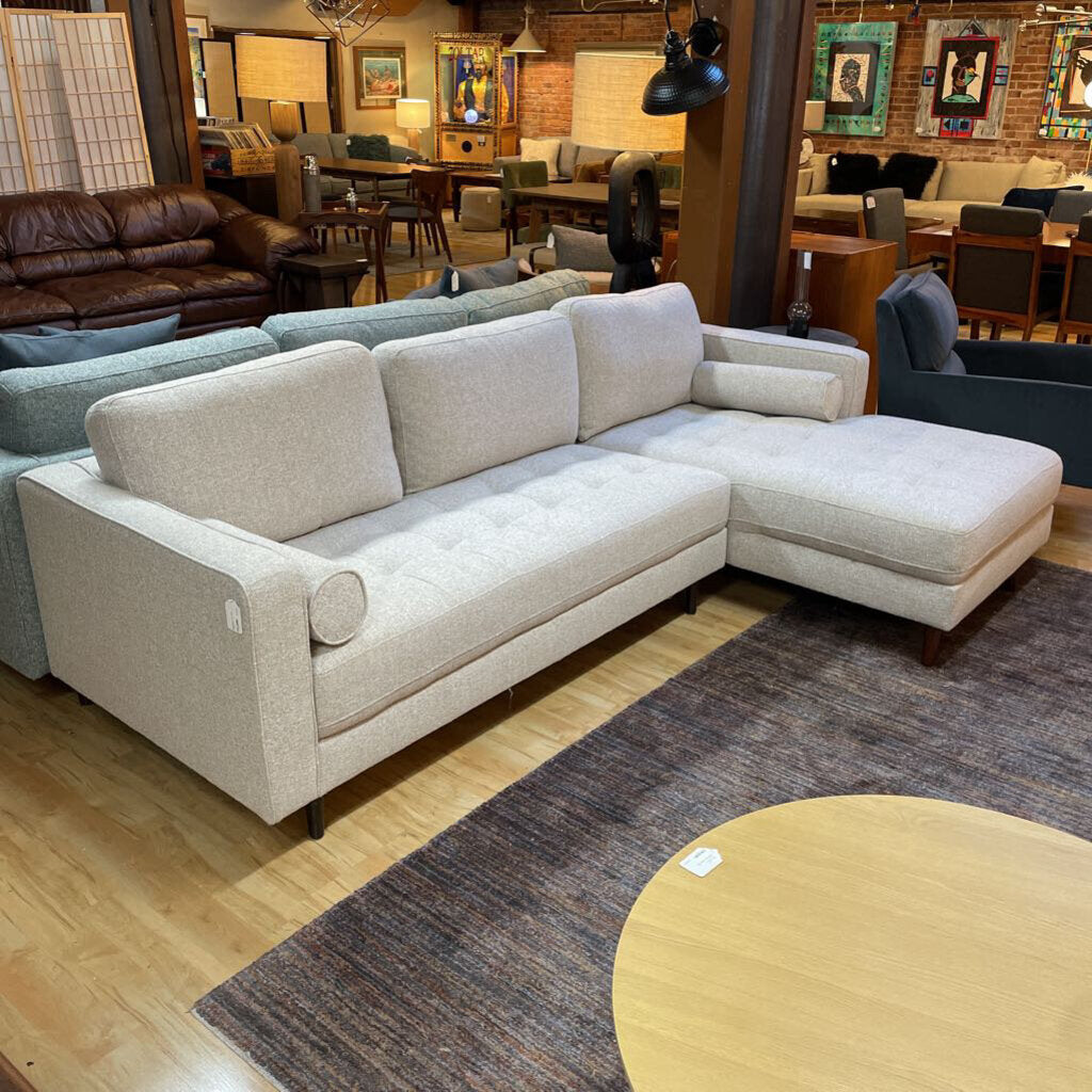 Beige sectional sofa in a furniture store with various other furniture pieces in the background.