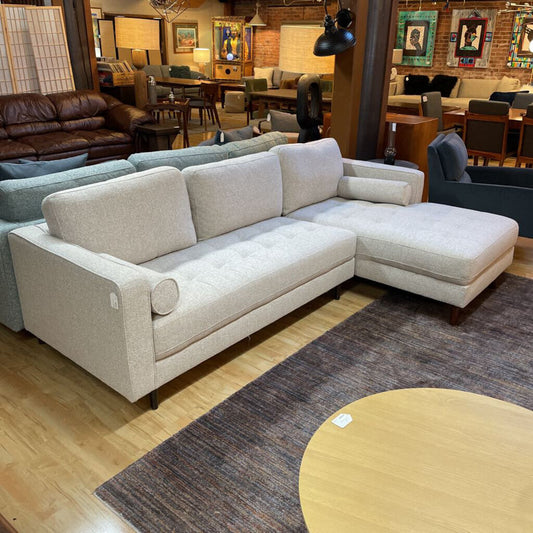 Beige sectional sofa in a furniture store with various other furniture pieces in the background.