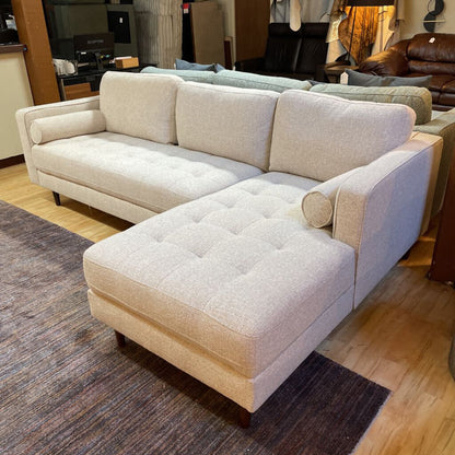 Beige sectional sofa with matching ottoman in a showroom setting