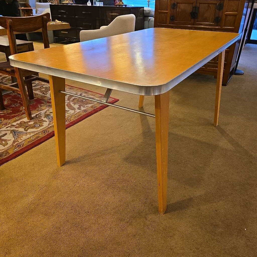 Wooden dining table with metal base in a room with chairs and carpeted floor.