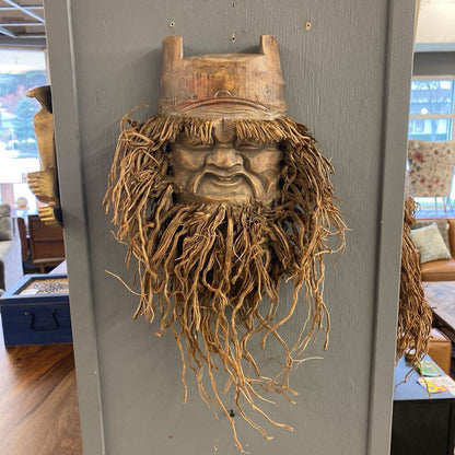 Wooden mask with roots hanging on a gray wall in a room with furniture.