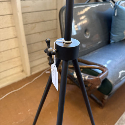 Black tripod stand with a tag in front of a gray sofa.