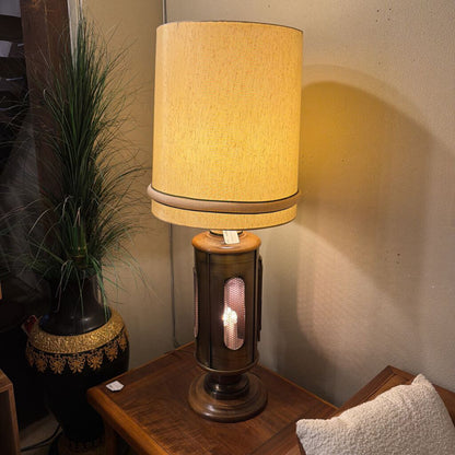 Table lamp with a textured beige shade on a wooden surface next to a plant.