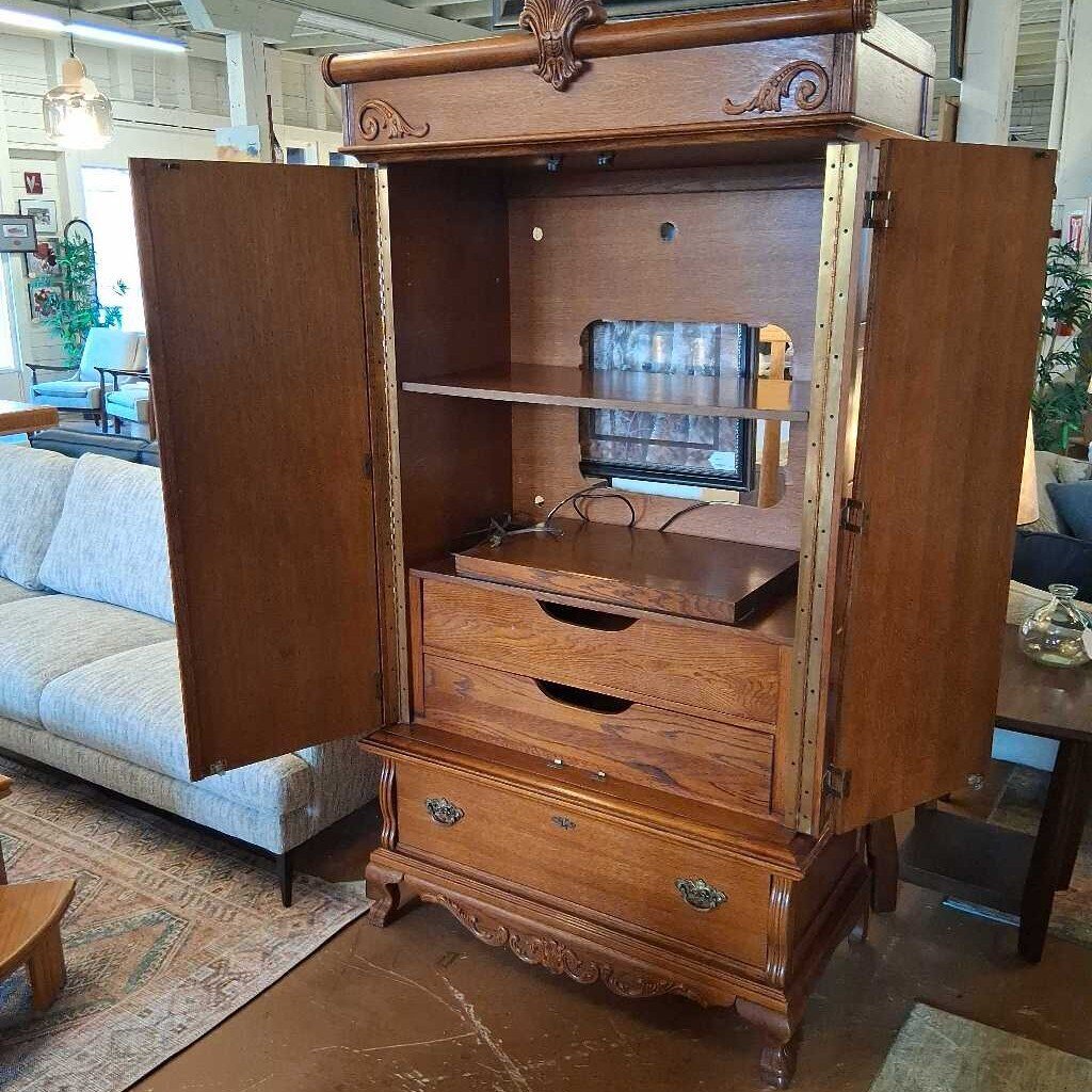 Wooden armoire with open doors in a room with furniture and decor.
