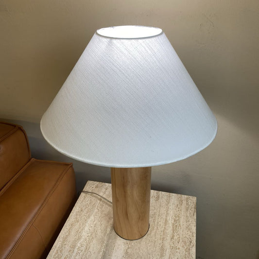 Table lamp with a white shade and wooden base on a table next to a brown leather couch.