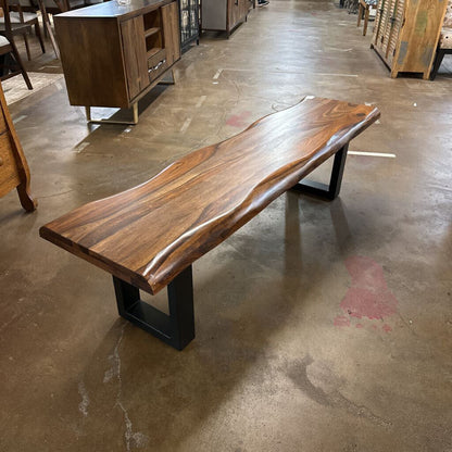 Wooden bench with a live-edge design on a concrete floor in a warehouse setting.