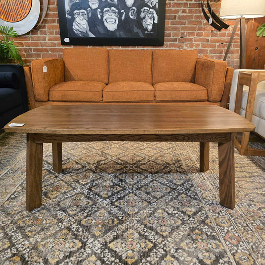 Brown sofa and wooden coffee table in a living room setting with a brick wall and artwork in the background.