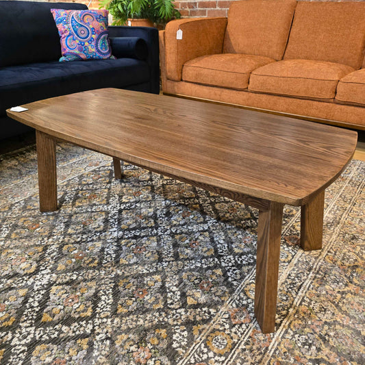 A rectangular dark wood coffee table with rounded corners and four square legs, resting on a grey and tan patterned rug