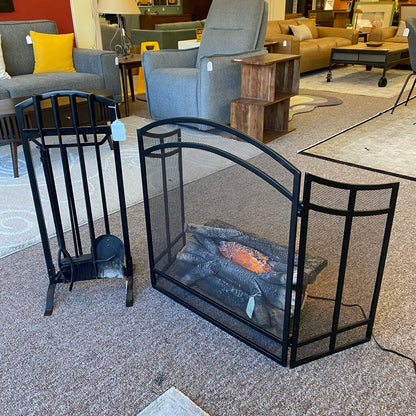 Black fireplace screen with logs inside, surrounded by furniture in a room setting.