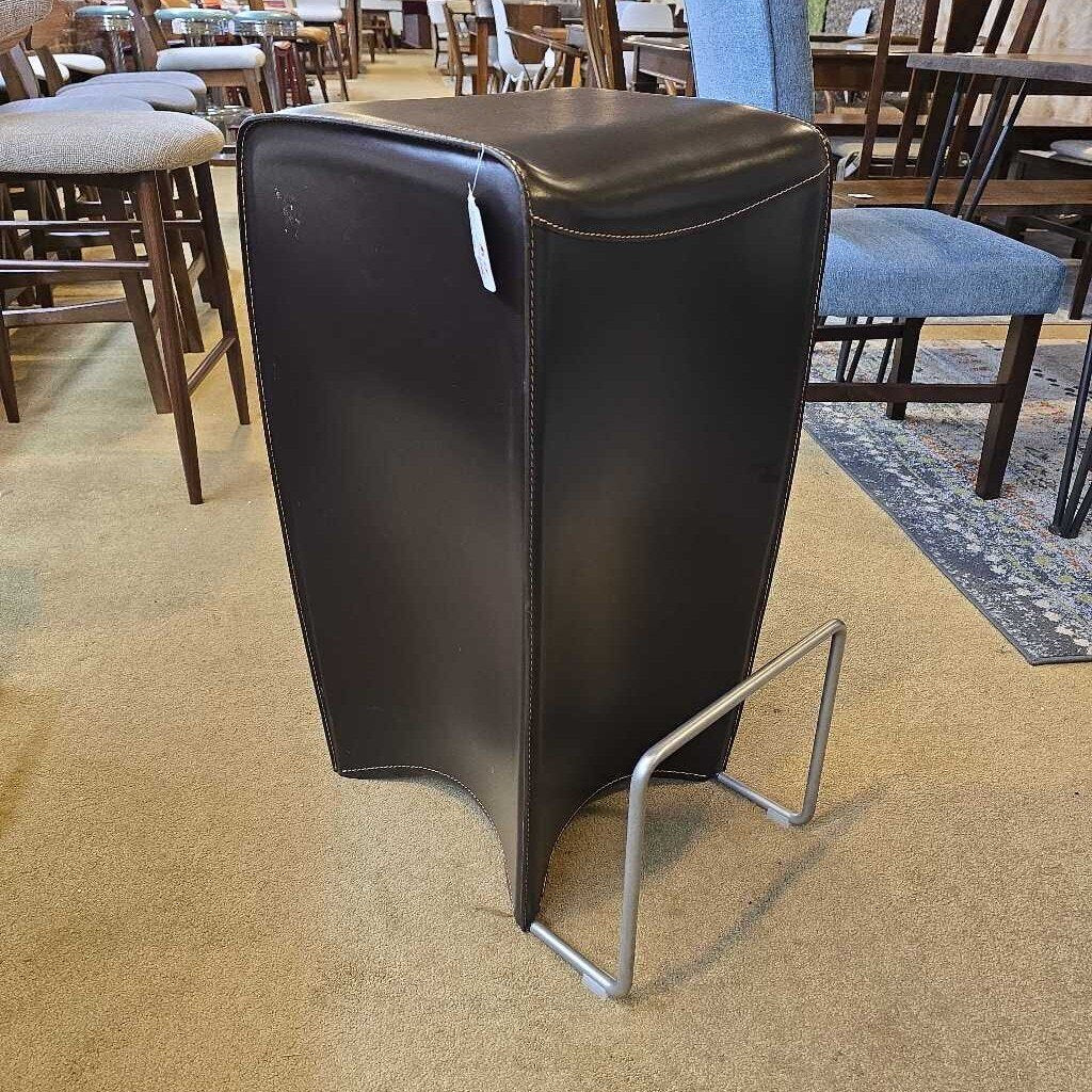 Black leather stool with metal legs on a carpeted floor in a store setting