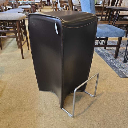 Black leather stool with metal legs on a carpeted floor in a store setting