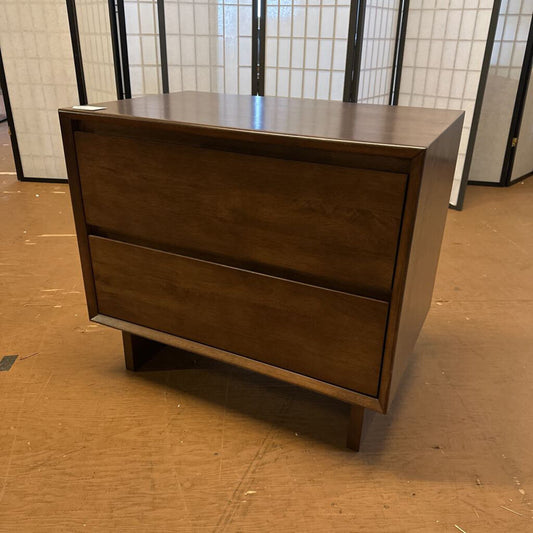 Wooden dresser with two drawers on a brown floor.