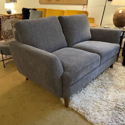 Gray sofa in a showroom with other furniture and decor items.