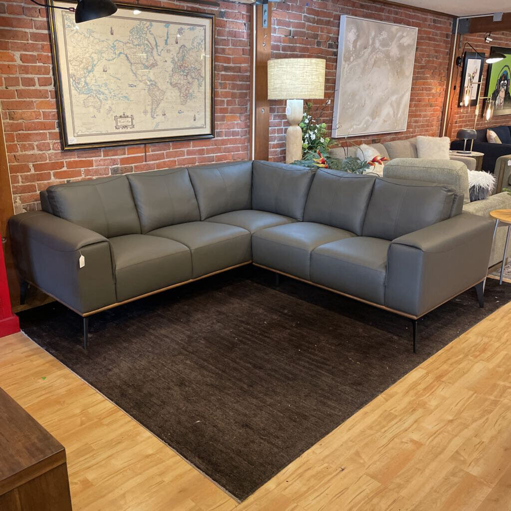 Gray sectional sofa in a living room with brick walls and framed maps.