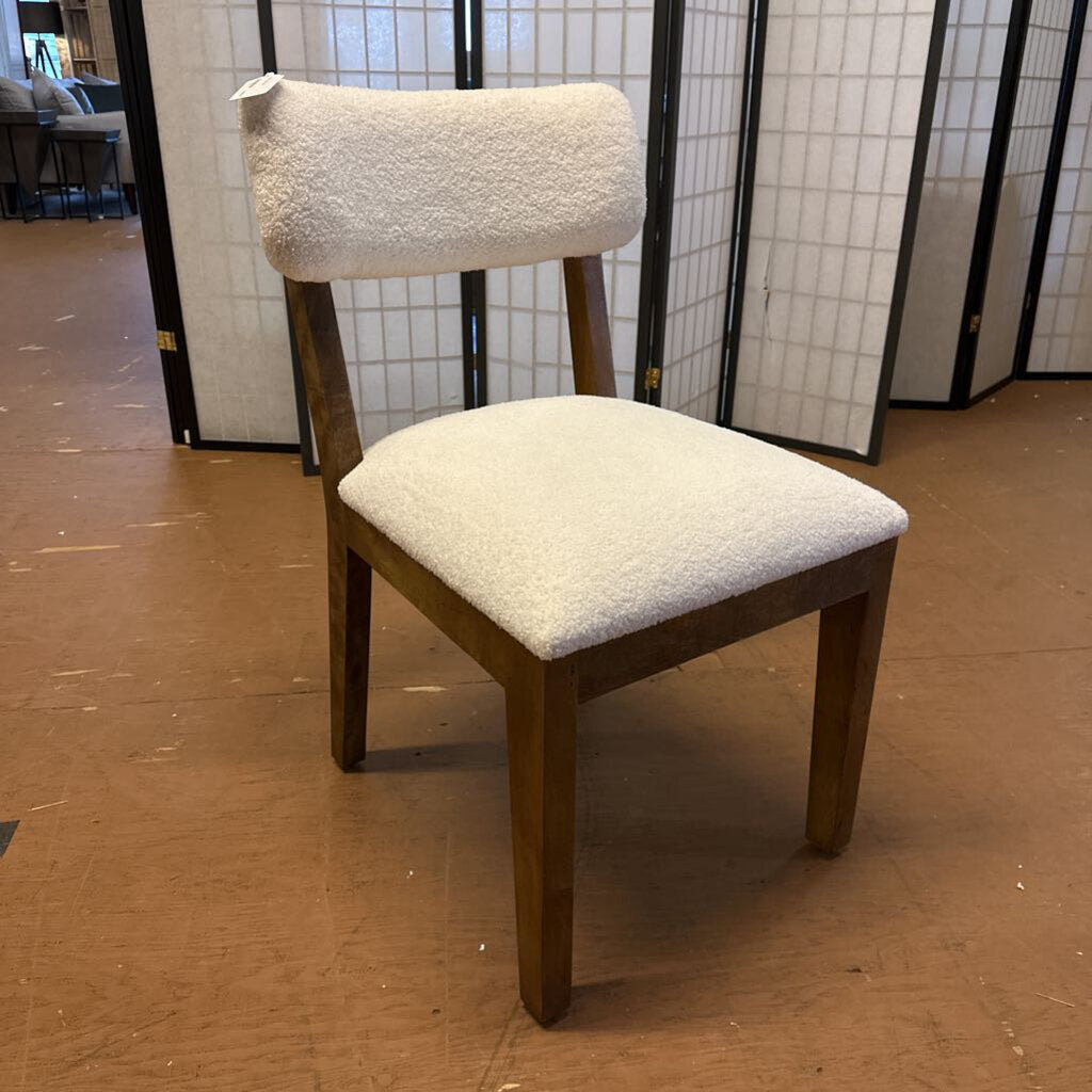 Wooden chair with white cushioned seat and backrest on a brown floor.