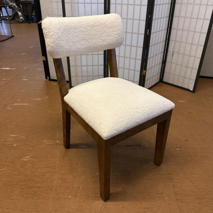 Chair with wooden frame and white cushioned seat and backrest on a brown floor.
