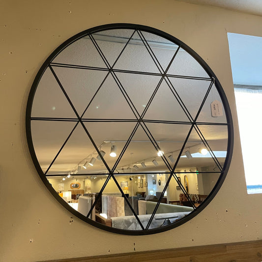 Round wall mirror with geometric black frame on a beige wall