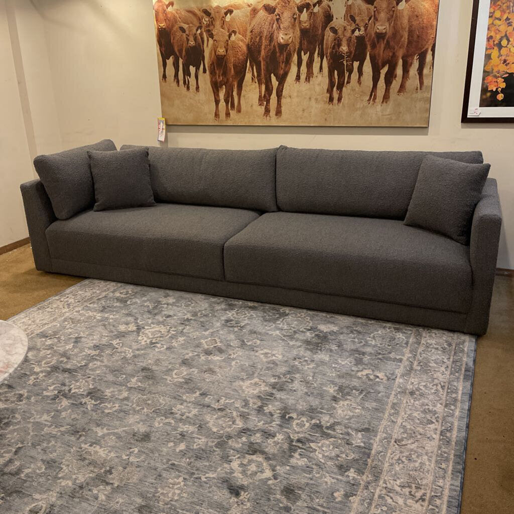 Gray sectional sofa in a room with a large painting of cows on the wall.