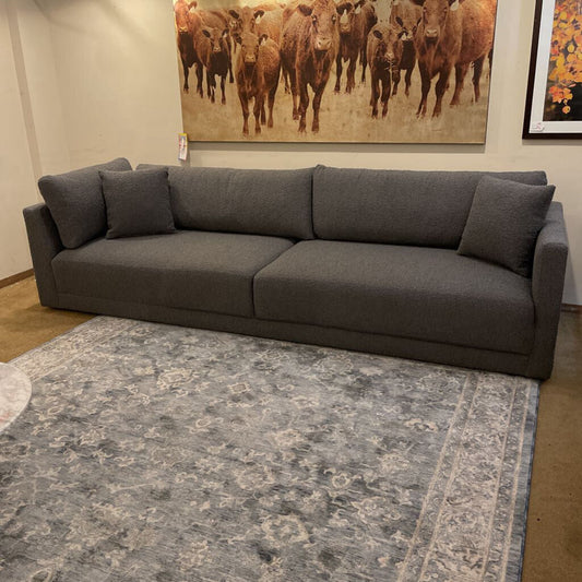 Gray sectional sofa in a room with a large painting of cows on the wall.