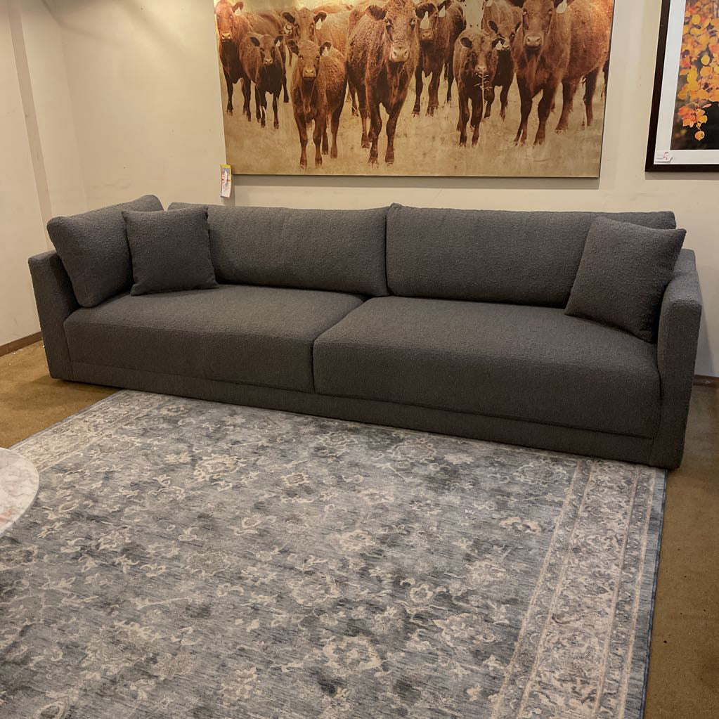 Gray sectional sofa in a room with a large rug and wall art of cows.